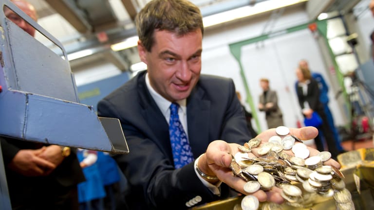 Markus Söder, damals bayerischer Finanzminister, wühlt in einer Kiste mit 2-Euromünzen des Motivs "Neuschwanstein": Hebammen, Pflegende und Eltern sollen Geld bekommen.