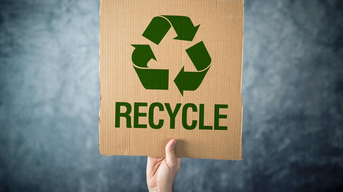 Eine Pappe mit der Aufschrift "Recycle" wird in die Luft gehalten: Die EU will bis 2030 einen Anstieg der Recyclingquote von 20 Prozent erreichen.