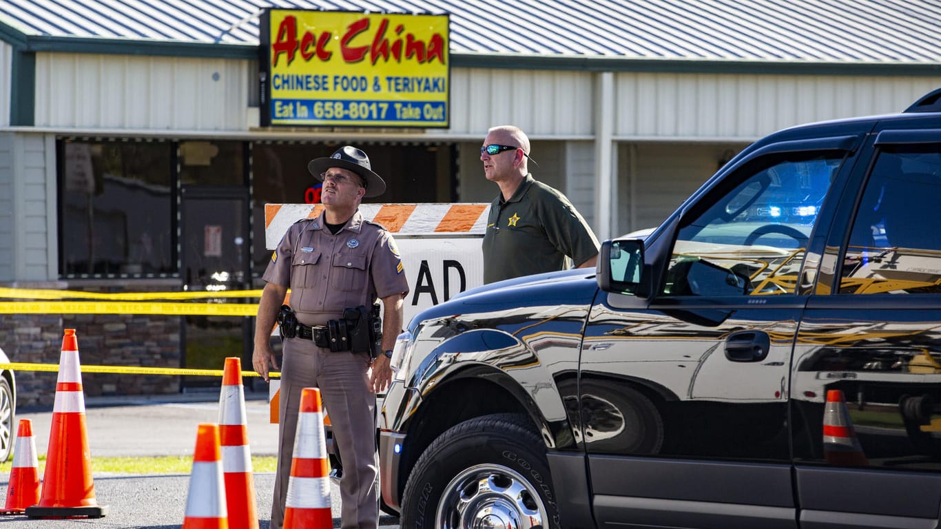 Zwei Polizisten in Trenton, Florida (USA) stehen vor einem "Ace China"-Restaurant und blicken in die Luft, während ein Hubschrauber über sie hinwegfliegt: In Trenton in Florida sind zwei Polizisten erschossen worden.