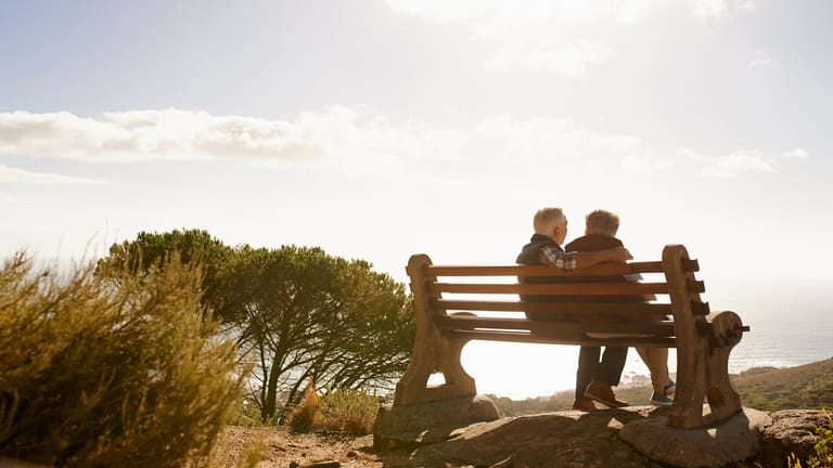 Ein älteres Paar auf einer Bank am Strand: Kapitalgedeckte Vorsorgemaßnahmen mit staatlicher Förderung können die gesetzliche Rente aufbessern.