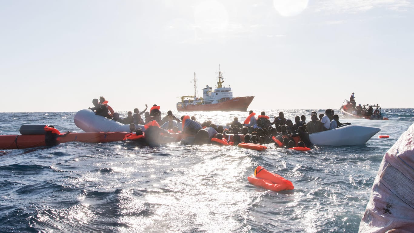 Zahlreiche Flüchtlinge werden während eines Rettungseinsatzes am vor der libyschen Küste geborgen: Im Hintergrund die "Aquarius" der Organisationen SOS Méditerranée und Ärzte ohne Grenzen.