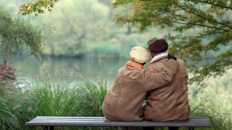 Älteres Paar sitzt auf einer Bank und schaut auf einen See: Um die Zeit im Alter in Ruhe zu genießen, bedarf es einiger Vorbereitung.