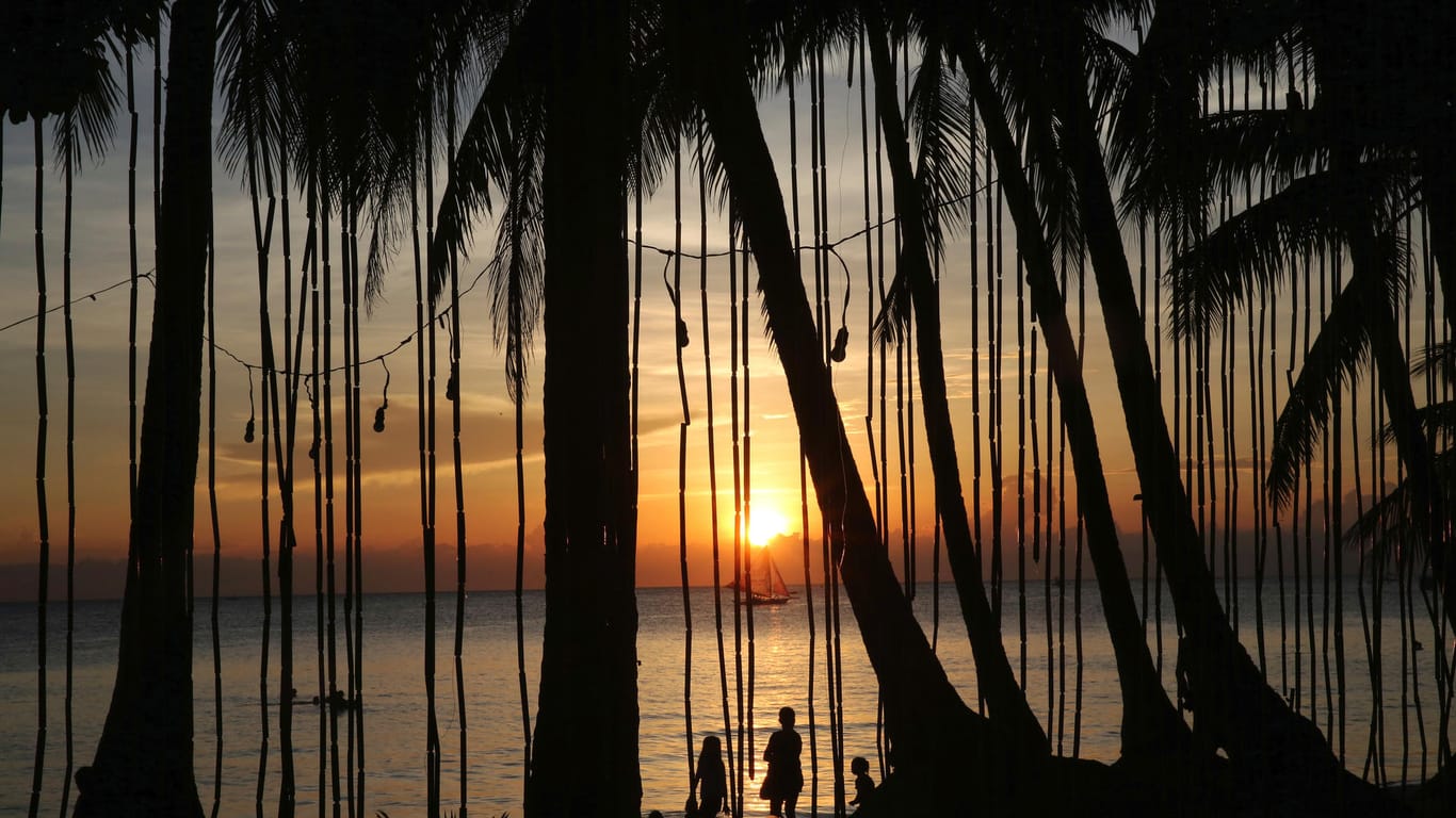 Insel Boracay (Philippinen): Menschen stehen bei Sonnenuntergang am Strand.