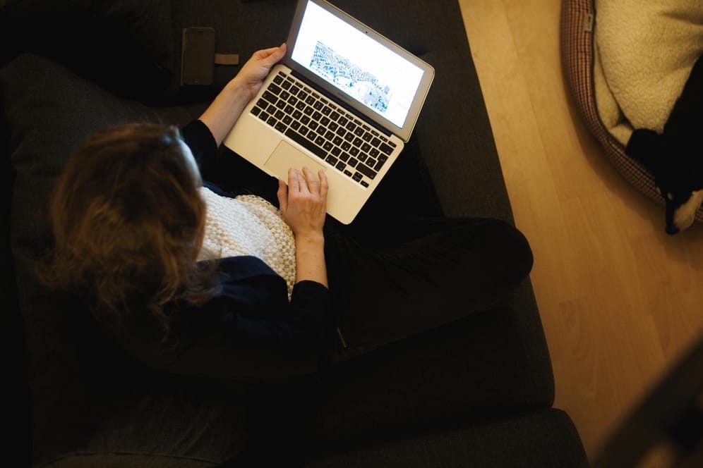 Eine Frau sitzt auf der Couch ihrer Wohnung und arbeitet am Laptop: FDP und Union wollen mit der Flexibilisierung der Arbeitszeit die Vereinbarkeit zwischen Beruf und Familie verbessern.