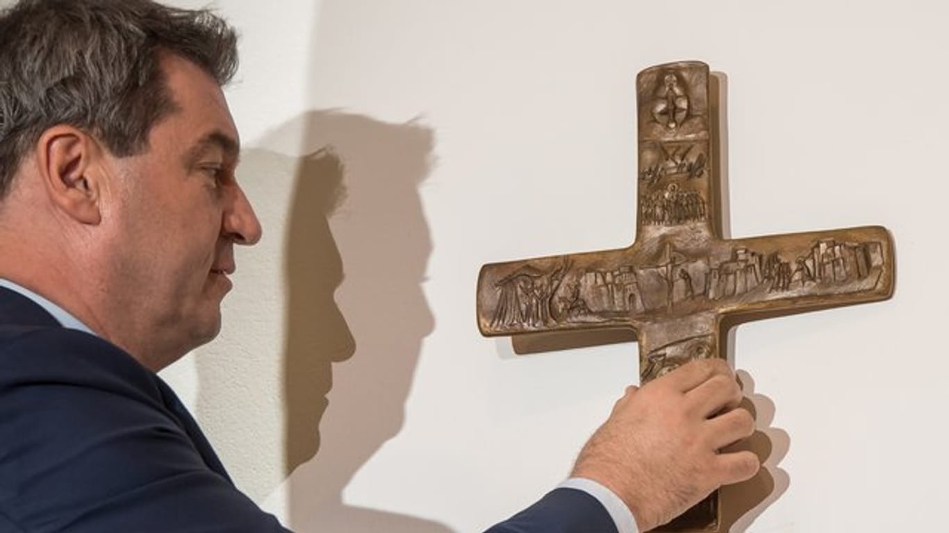 Bayerns Ministerpräsident Markus Söder hängt ein Kreuz im Eingangsbereich der bayerischen Staatskanzlei auf.