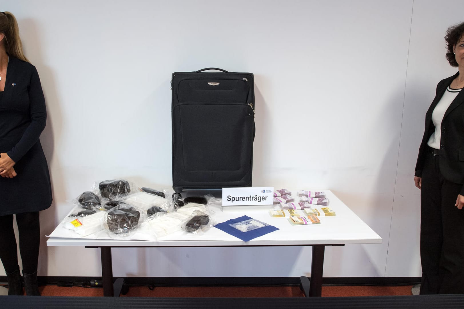 Opium, Kokain, Christal Meth und Geldbündel liegen von Polizistinnen bewacht neben einem Koffer als Spurenträger auf einem Tisch: Ermittler haben einen internationalen Drogenring zerschlagen, bei dem die Kuriere überwiegend aus Nordrhein-Westfalen stammen.