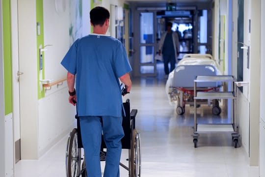 Ein Pfleger schiebt einen Rollstuhl.