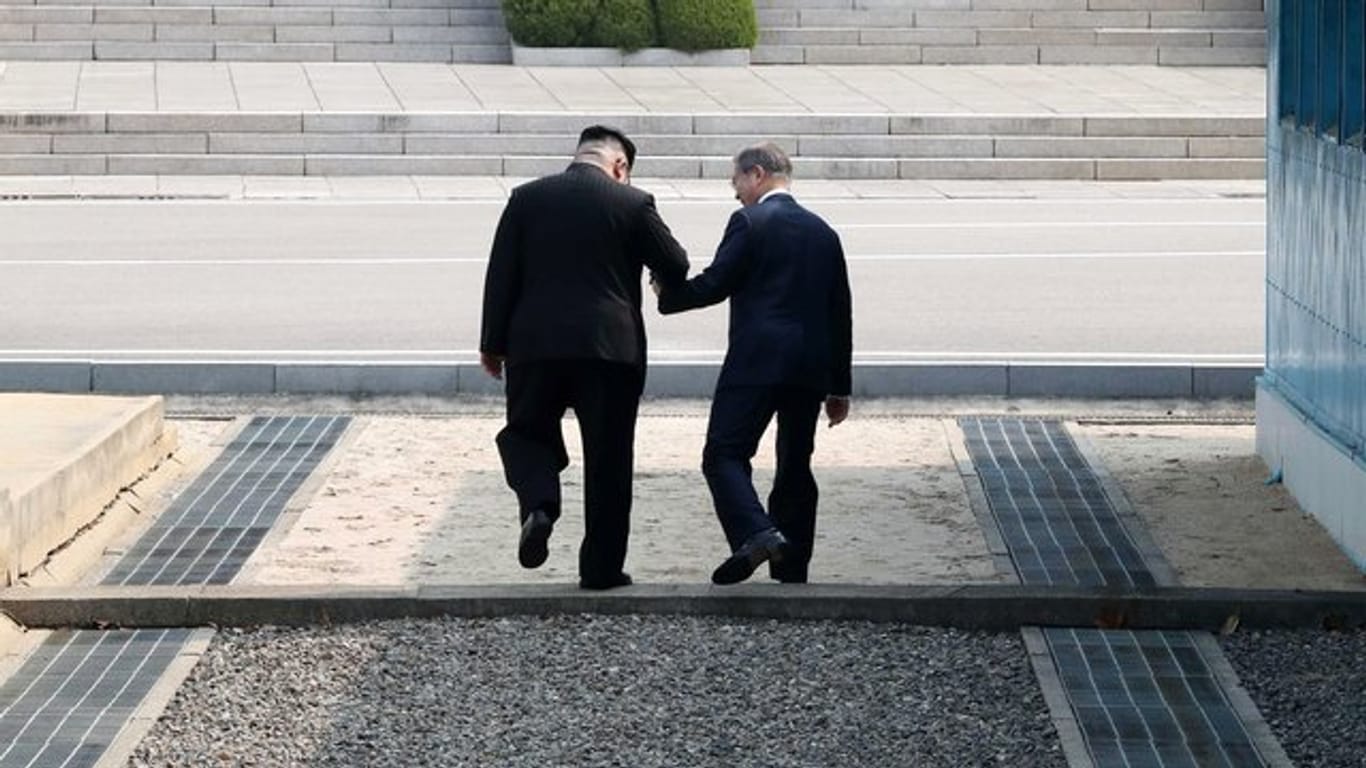 Kim Jong Un (L), Machthaber von Nordkorea, und Moon Jae In, Präsident von Südkorea, gehen Hand in Hand über die Betonschwelle, die die Grenze zwischen ihren Ländern markiert.