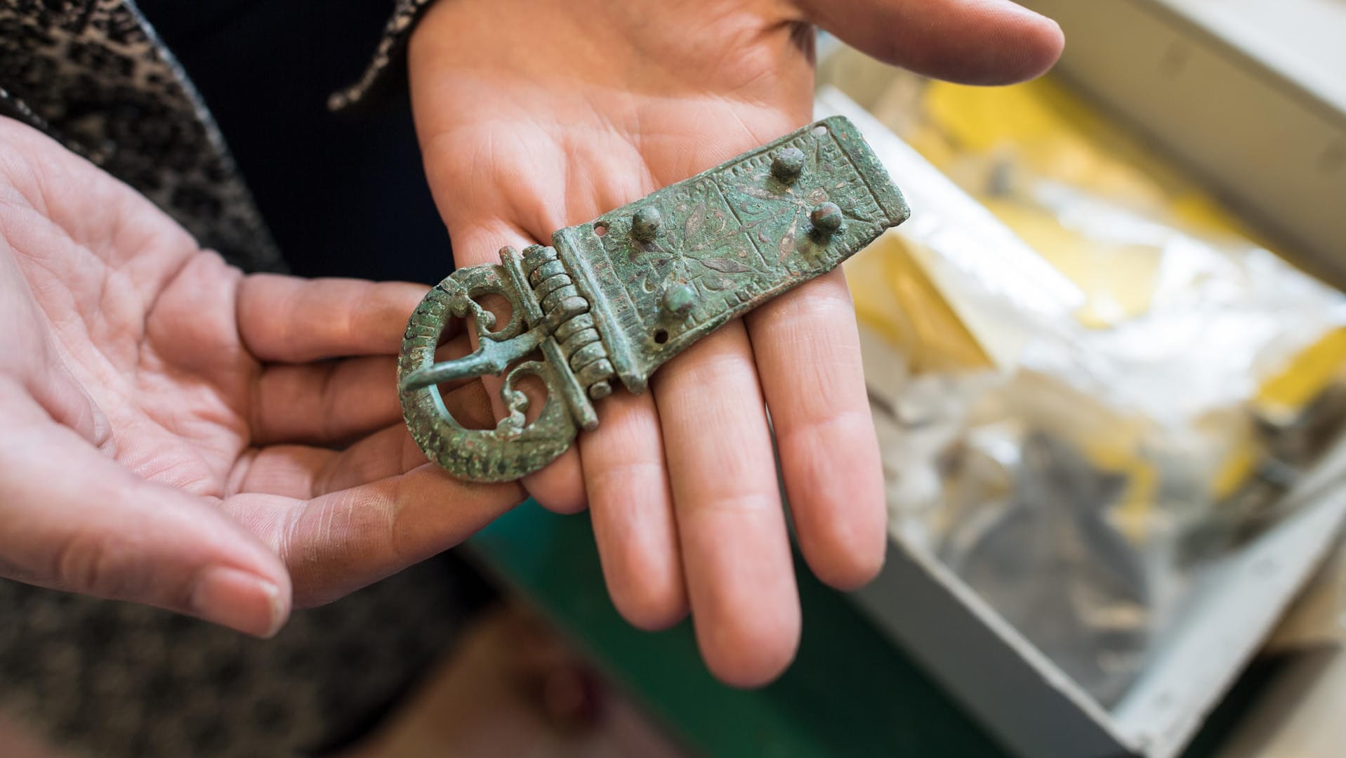 Eine Mitarbeiterin des Museums Burg Linn hält die Gürtelschnalle eines römischen Soldaten in den Händen: In Krefeld wurden unter anderem Helme, Münzen und Pferdeskelette gefunden.