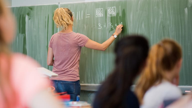 Eine Lehrerin schreibt an eine Schultafel: Laut einer Studie erfahren Lehrer an jeder dritten Grundschule körperliche Gewalt.