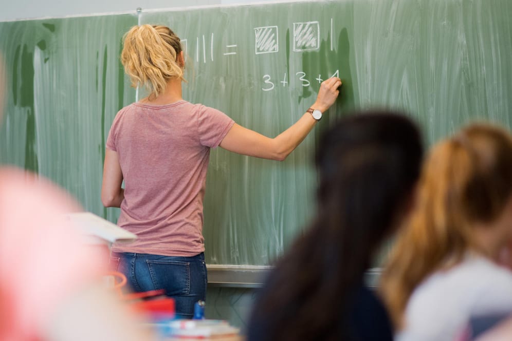 Eine Lehrerin schreibt an eine Schultafel: Laut einer Studie erfahren Lehrer an jeder dritten Grundschule körperliche Gewalt.