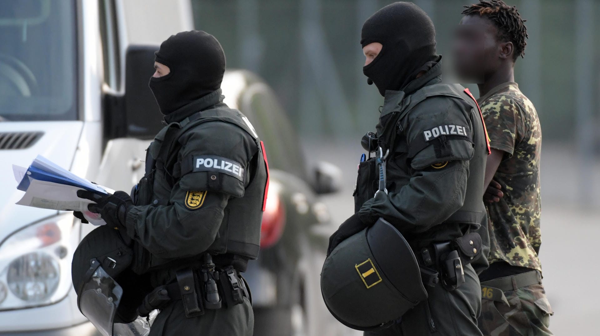 In der Landeserstaufnahmeeinrichtung für Flüchtlinge (LEA) wird ein Mann von maskierten Polizisten eskortiert: Nachdem es bei der gescheiterten Abschiebung eines 23-jährigen Togolesen vor vier Tagen zu Ausschreitungen gekommen war, läuft ein Großeinsatz der Polizei in der Flüchtlingsunterkunft.