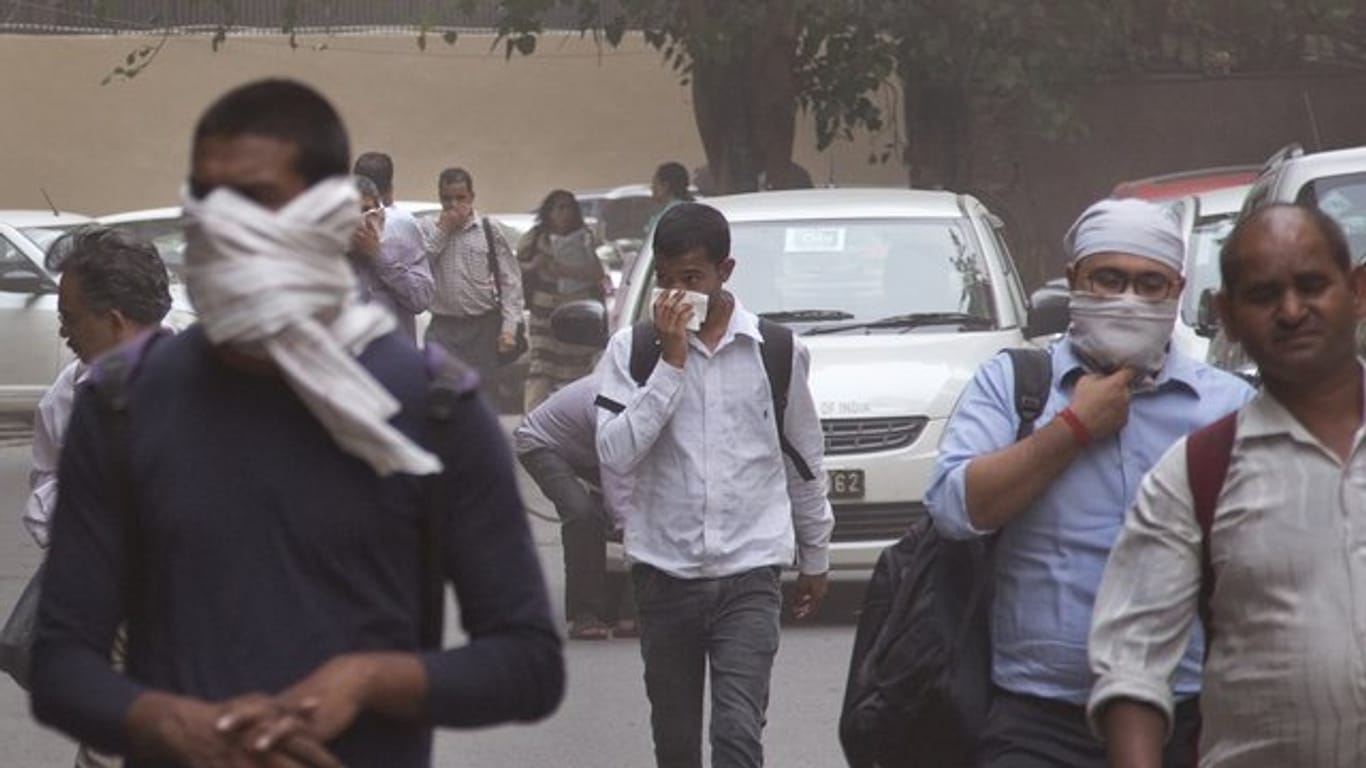 Leute schützen sich in Neu Delhi mit Tüchern vor einem Staubsturm.