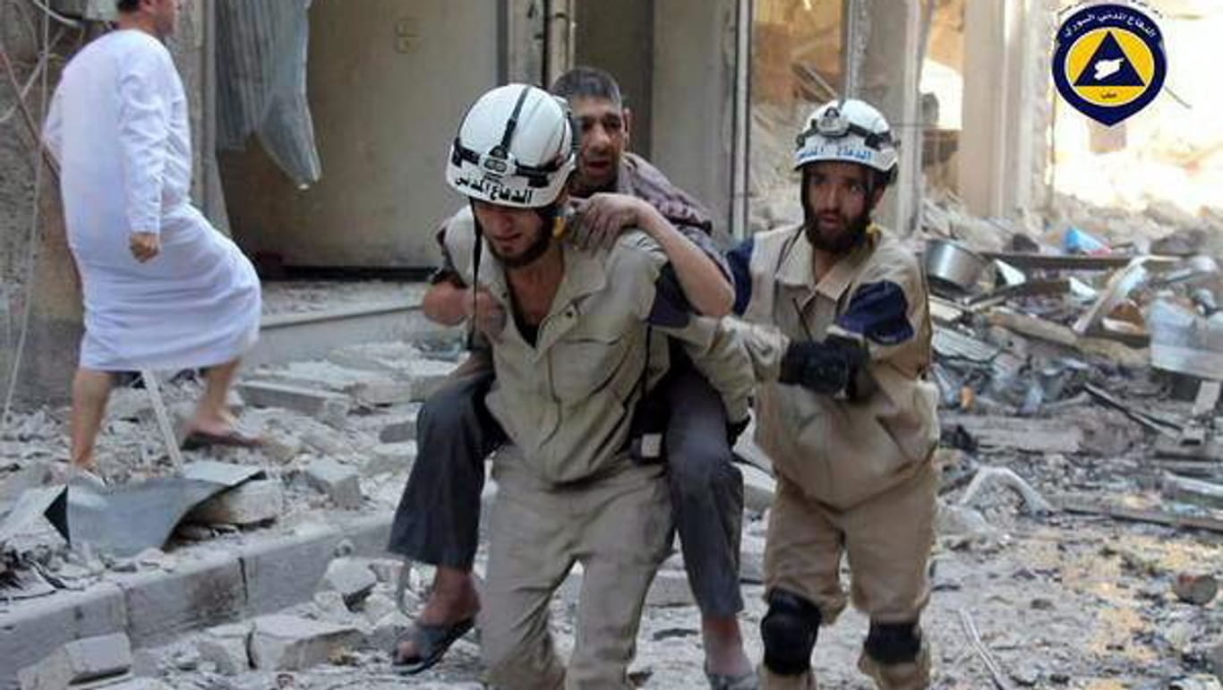 Ein Weißhelm trägt einen Verwundeten durch die Trümmer der syrischen Stadt Aleppo (Archiv)