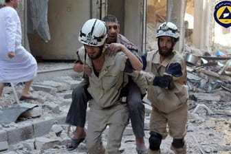 Ein Weißhelm trägt einen Verwundeten durch die Trümmer der syrischen Stadt Aleppo (Archiv)