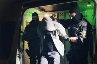 Polizisten führen in Hamburg einen im Rahmen der Razzia vorläufig festgenommenen Verdächtigen ab.