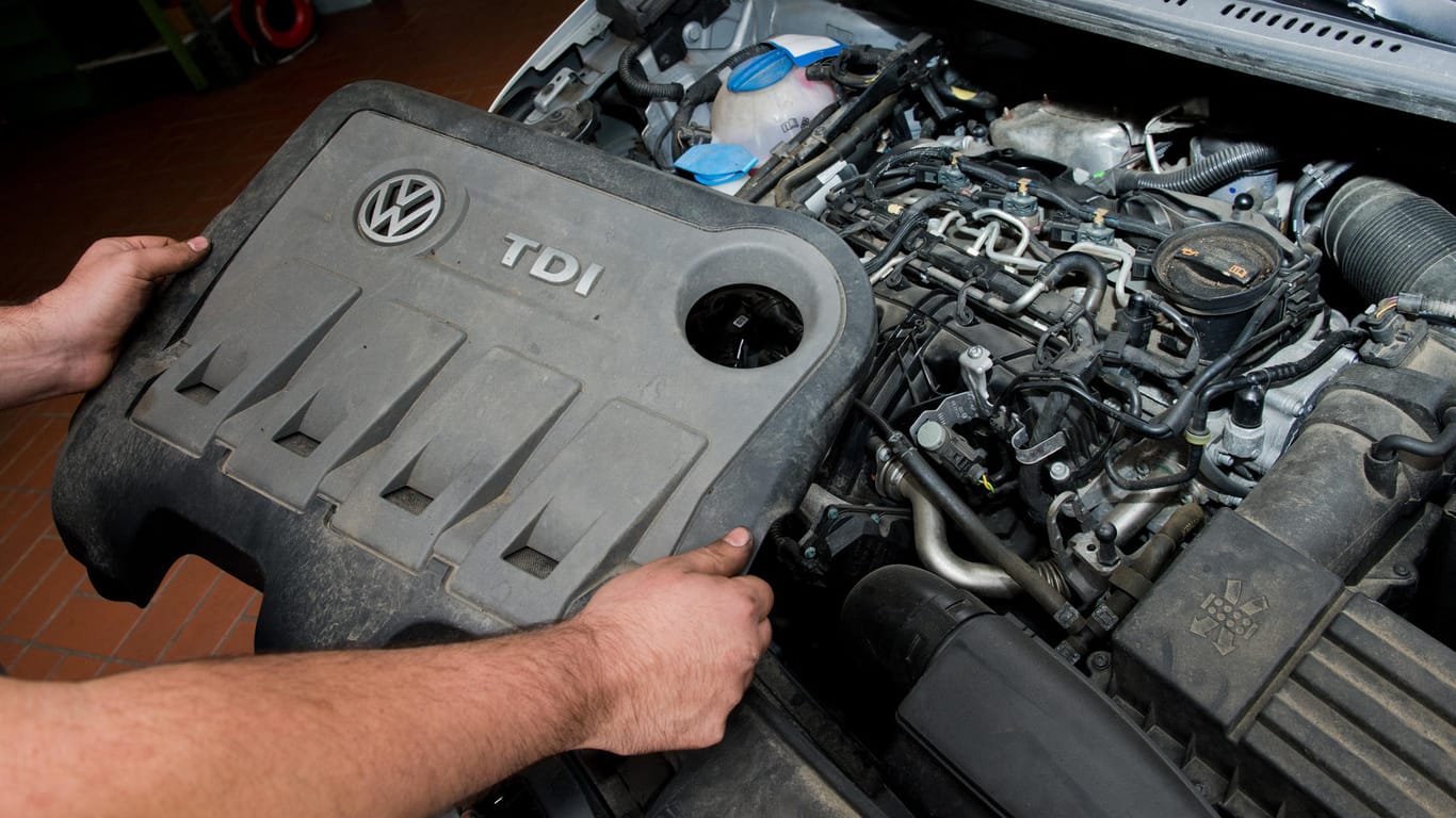 Ein KFZ-Servicetechniker in einer Autowerkstatt hält die Abdeckung vor einem vom Abgas-Skandal betroffenen Dieselmotor: Expertengruppe sieht Zwang zur Diesel-Nachrüstung für unmöglich.