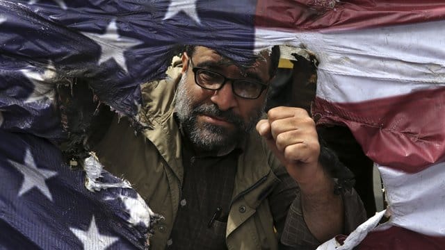 Ein Demonstrant ballt bei einem Protest gegen die USA in Teheran seine Faust hinter einer verbrannten US-Flagge. Ein Demonstrant ballt bei einem Protest gegen die USA in Teheran seine Faust hinter einer verbrannten US-Flagge.