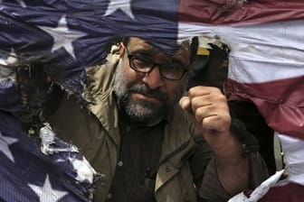 Ein Demonstrant ballt bei einem Protest gegen die USA in Teheran seine Faust hinter einer verbrannten US-Flagge.