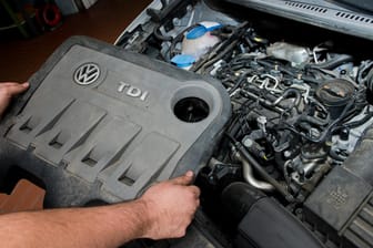 Dieselkrise: Ein KFZ-Servicetechniker in einer Autowerkstatt hält die Abdeckung vor einem vom Abgas-Skandal betroffenen 2.0l TDI Dieselmotor.