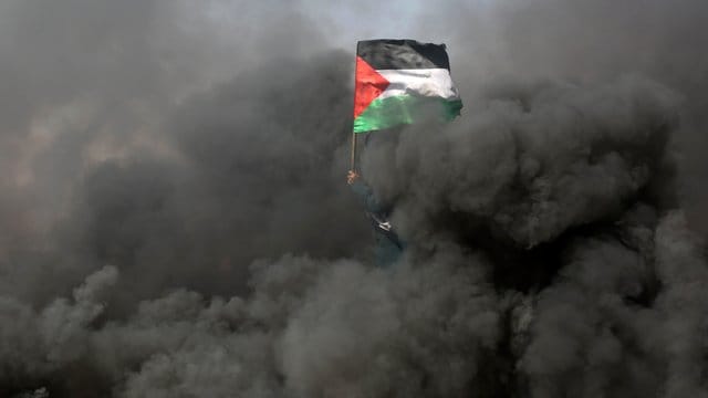 Eine Frau schwenkt bei Protesten an der Grenze zu Israel im Gazastreifen inmitten von Rauchschwaden eine palästinensische Flagge. Eine Frau schwenkt bei Protesten an der Grenze zu Israel im Gazastreifen inmitten von Rauchschwaden eine palästinensische Flagge.