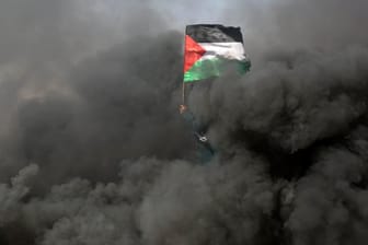 Eine Frau schwenkt bei Protesten an der Grenze zu Israel im Gazastreifen inmitten von Rauchschwaden eine palästinensische Flagge.