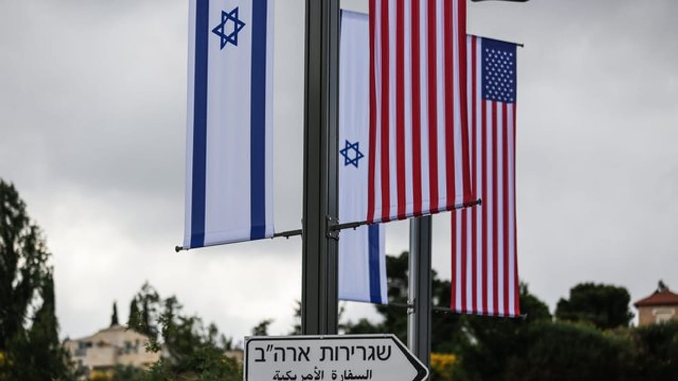 Eine israelische und eine us-amerikanische Flagge hängen über einem Schild, das den Weg zur Botschaft der USA in Jerusalem weist.