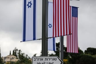 Eine israelische und eine us-amerikanische Flagge hängen über einem Schild, das den Weg zur Botschaft der USA in Jerusalem weist.