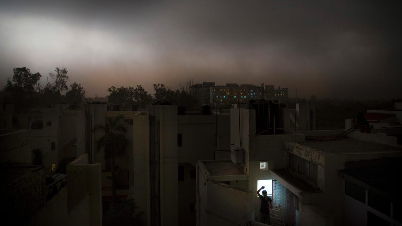 Ein Mann in Neu Delhi steht auf dem Balkon eines Apartments während eines plötzlichen Sturms: In Indiens Hauptstadt sind zwei Menschen bei schweren Gewittern gestorben.