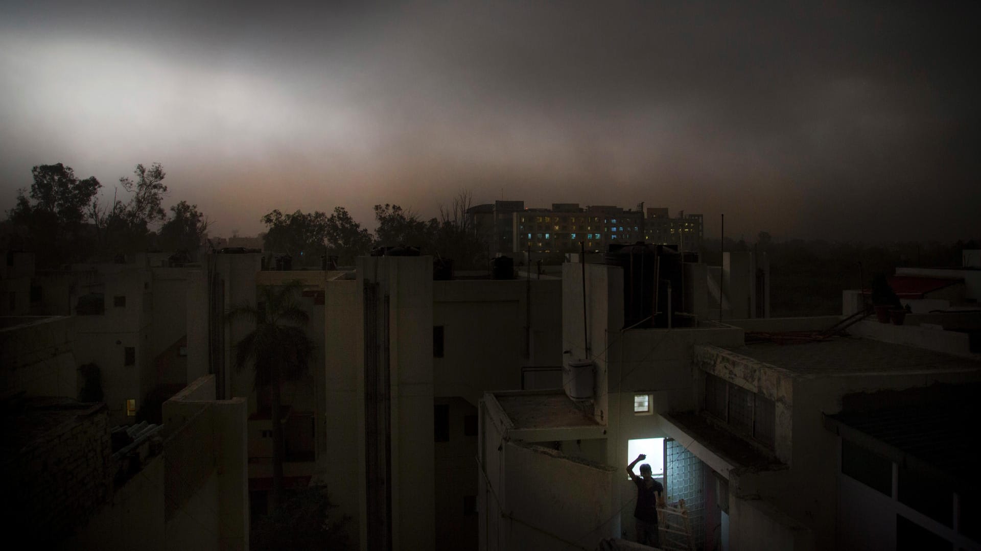 Ein Mann in Neu Delhi steht auf dem Balkon eines Apartments während eines plötzlichen Sturms: In Indiens Hauptstadt sind zwei Menschen bei schweren Gewittern gestorben.