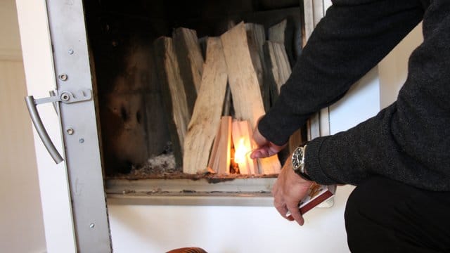 Ein Mann zündet den Kamin an: Ältere Öfen stoßen vergleichsweise viele Emissionen aus. Sie werden daher seit Jahren schrittweise neuen Grenzwerten unterworfen.