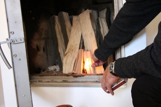 Ein Mann zündet den Kamin an: Ältere Öfen stoßen vergleichsweise viele Emissionen aus. Sie werden daher seit Jahren schrittweise neuen Grenzwerten unterworfen.