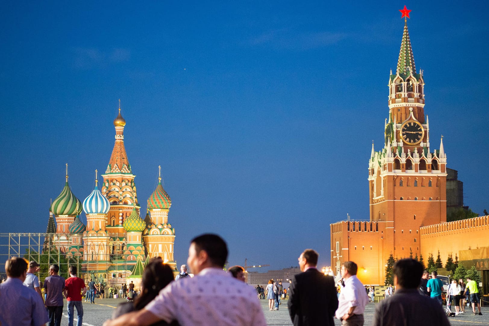 Moskau in Russland: Besucher spazieren zur blauen Stunde auf dem Roten Platz. Links steht die Basilius-Kathedrale und rechts das Lenin-Mausoleum und der Moskauer Kreml.