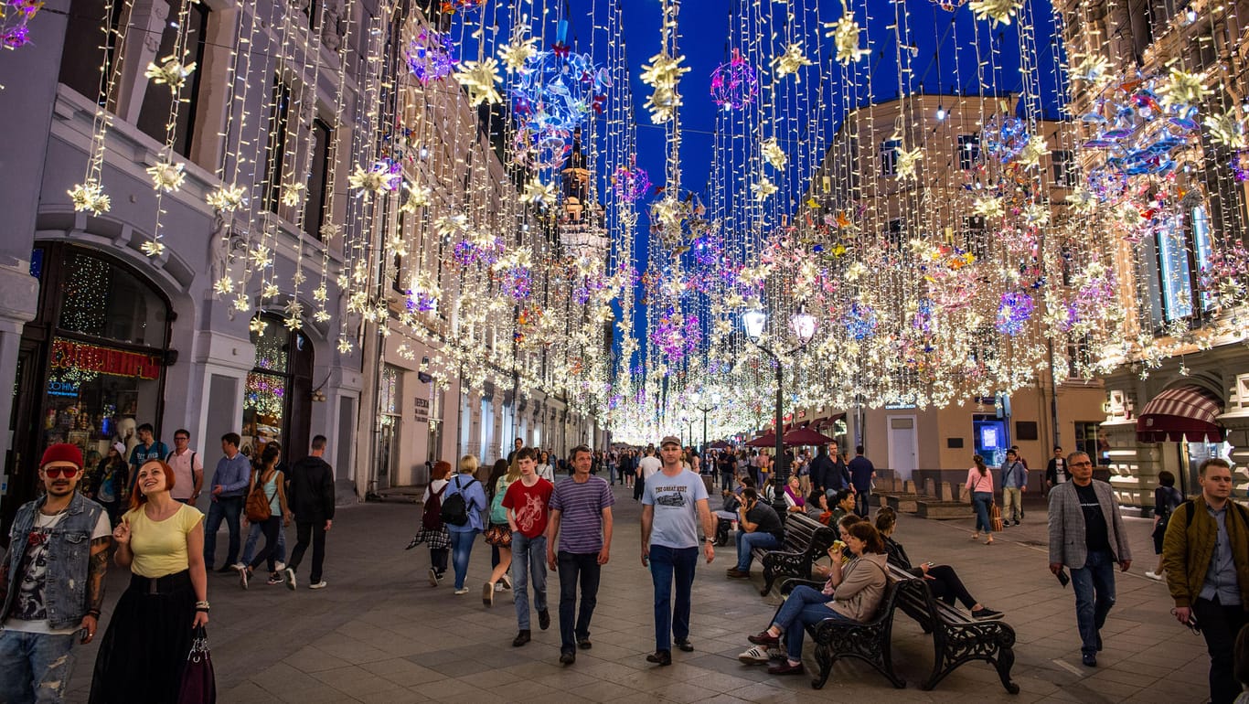 Moskau: Besucher spazieren auf einer Einkaufsstraße neben dem Roten Platz. Zur Beleuchtung wurden Lichterketten aufgehängt.