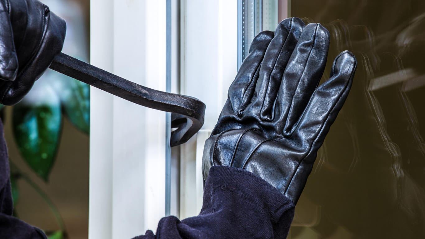 Einbrecher hebelt ein Fenster mit einem Brecheisen auf: Urlauber sollten an ihrem Haus oder ihrer Wohnung keine Hinweise auf ihre Abwesenheit geben. Diese könnten Einbrecher geradezu einladen.