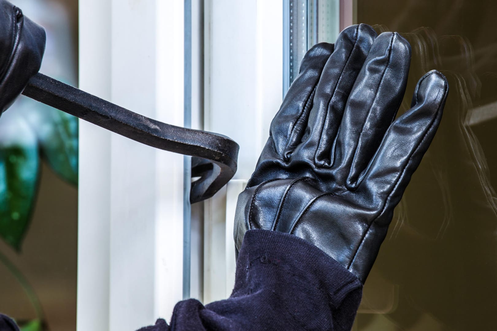 Einbrecher hebelt ein Fenster mit einem Brecheisen auf: Urlauber sollten an ihrem Haus oder ihrer Wohnung keine Hinweise auf ihre Abwesenheit geben. Diese könnten Einbrecher geradezu einladen.