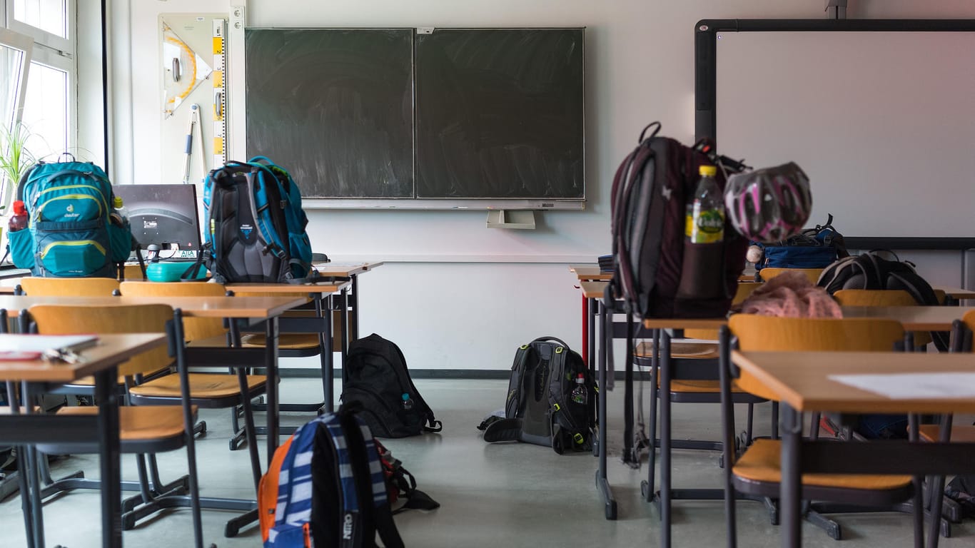 Zwei Schulranzen stehen auf einer Schulbank in einem leeren Klassenraum: Welche Bußgelder drohen beim Schwänzen?