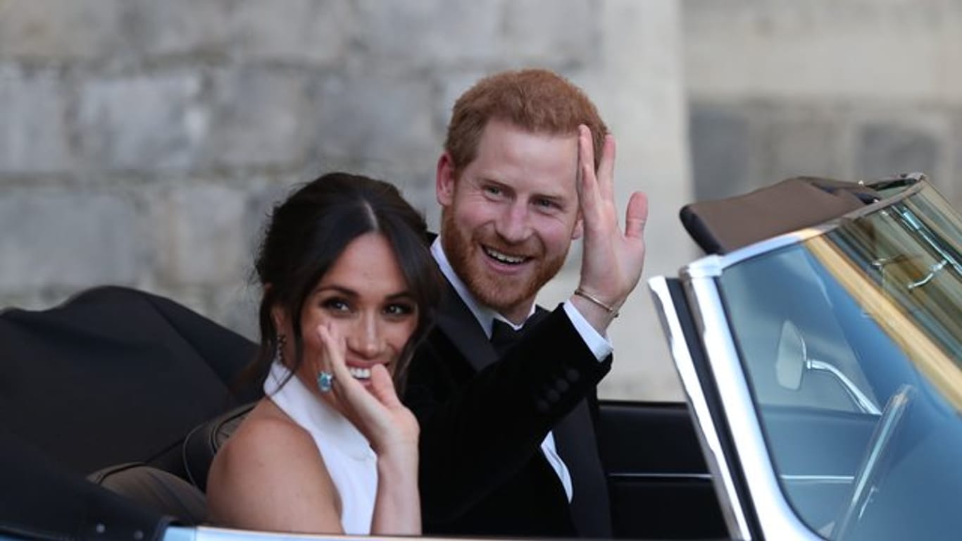 Der britische Prinz Harry und seine Frau Meghan winken aus dem Cabrio.