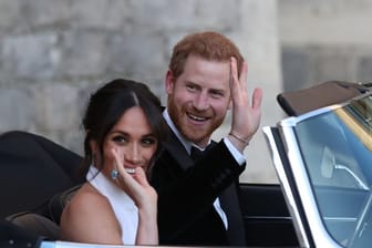 Der britische Prinz Harry und seine Frau Meghan winken aus dem Cabrio.