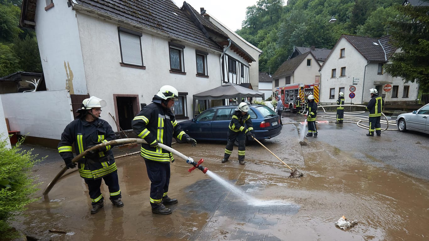 Feuerwehrleute säubern einen Gehweg und eine Straße vom Schlamm in Isenburg (Rheinland-Pfalz): Nach einem heftigen Gewitter sind Straßen und Keller überflutet.