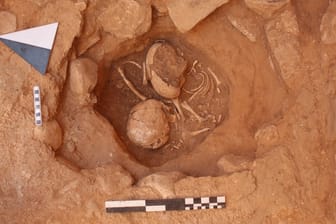 Archäologischer Fund: Grubenbestattung mit gegenüber hockendem Baby und Kleinkind unter dem Fußboden eines Hausraums in Baʻja.