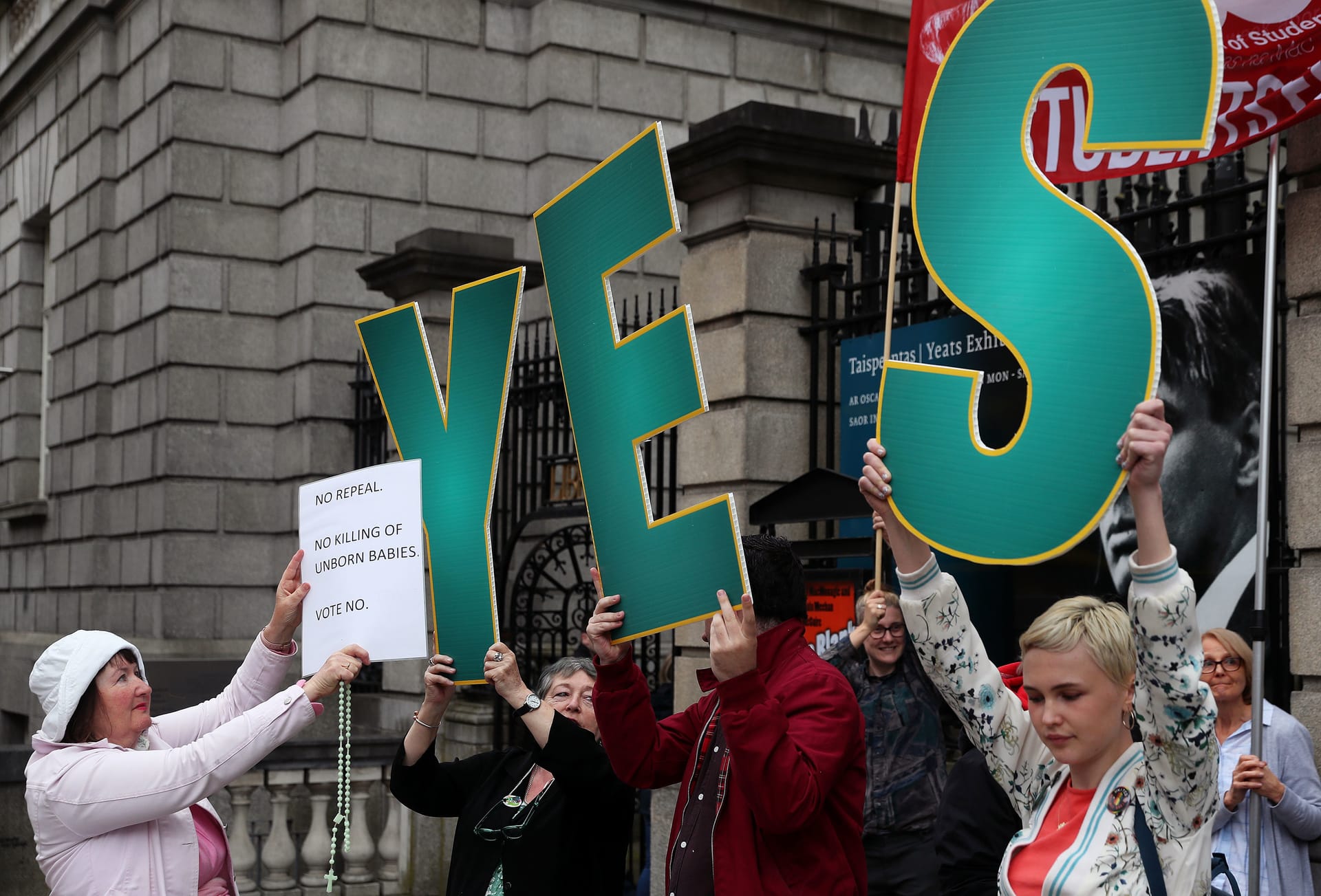 Eine Abtreibungsgegnerin (l.) hält ein weißes Blatt vor das "YES" von drei Frauen, die Abtreibungen befürworten.