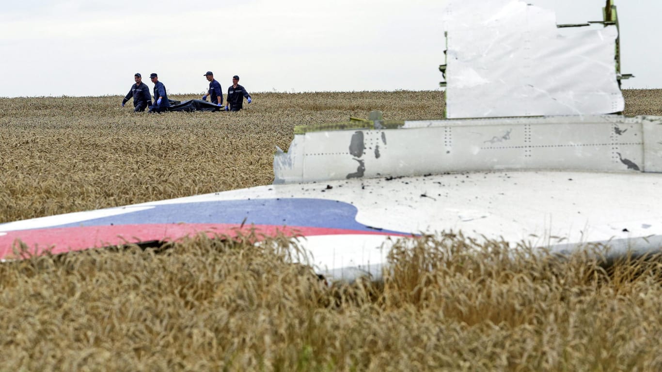 Einsatzkräfte tragen zwischen Trümmerteilen von Flug MH17 einen Leichnam davon. Kurz vor der Fußball-WM haben sich Angehörige mit einem offenen Brief an das russische Volk gerichtet.