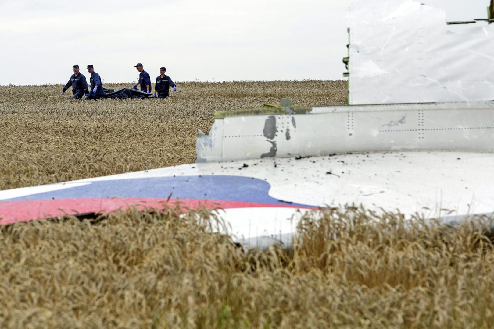 Einsatzkräfte tragen zwischen Trümmerteilen von Flug MH17 einen Leichnam davon. Kurz vor der Fußball-WM haben sich Angehörige mit einem offenen Brief an das russische Volk gerichtet.