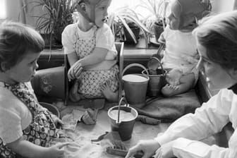 Medizin-Skandal: Contergan-geschädigte Kinder spielen mit einer Betreuerin in einem Sandkasten.