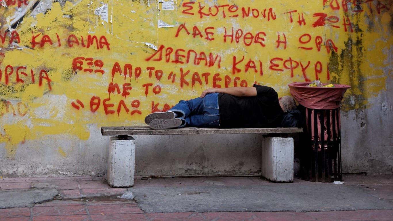 Piräus (Griechenland). im Hafenviertel: Ein Mann liegt auf einer Bank und schläft: Griechenland hat die höchste Staatsverschuldung im Euroraum.