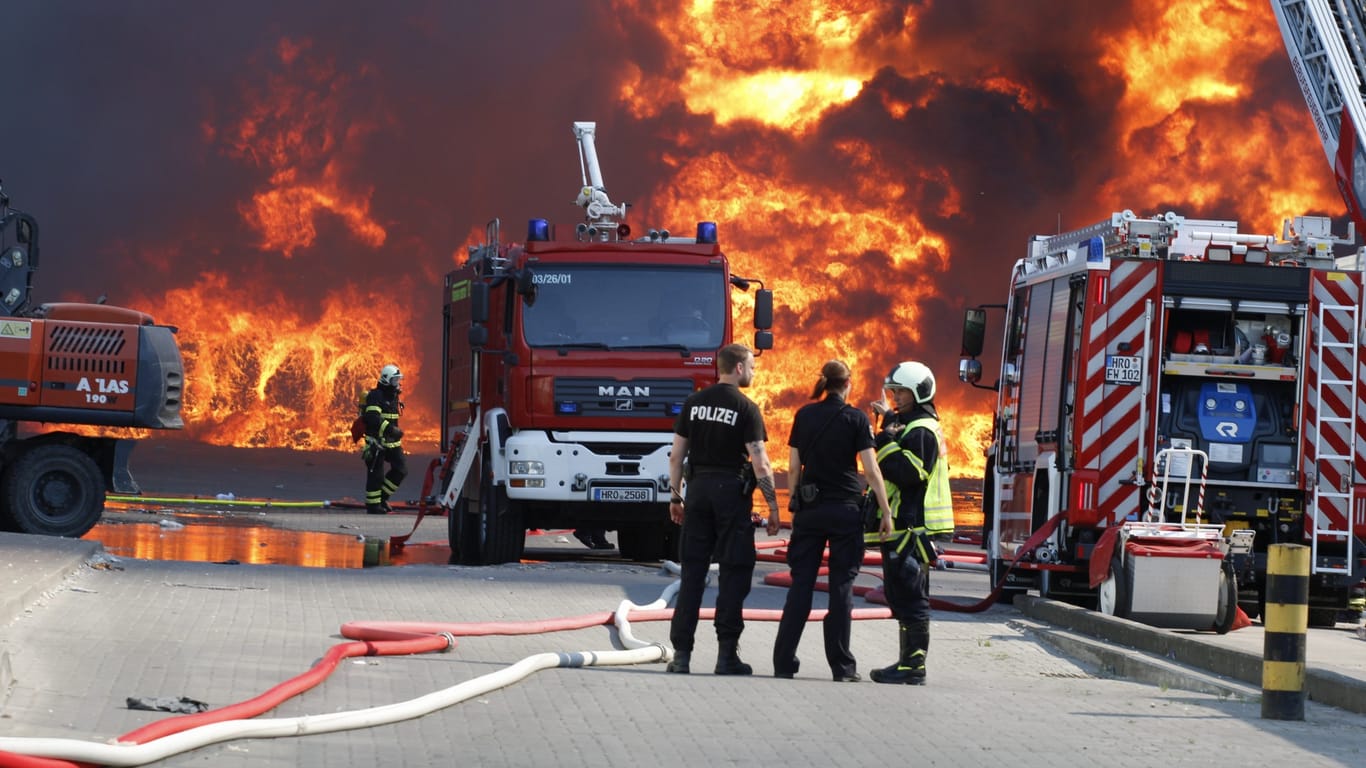 Einsatzkräfte der Polizei und Feuerwehr stehen bei dem Brand auf dem Gelände eines Entsorgungsunternehmens: Das Feuer konnte unter Kontrolle gebracht werden.