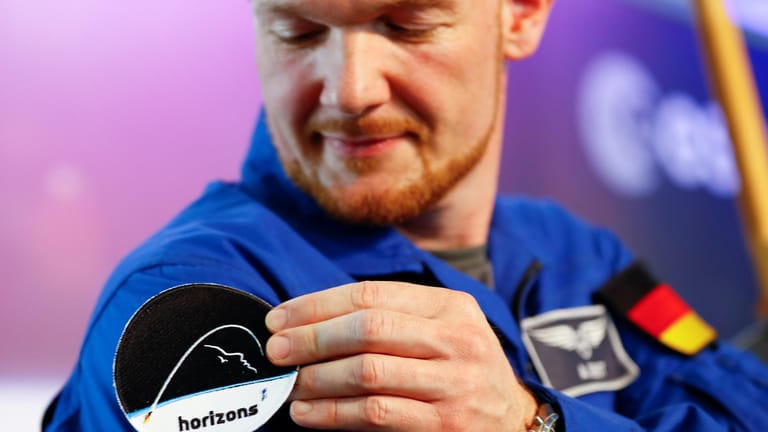 Mission "Horizons": Alexander Gerst klebt sich einen Button mit dem Logo seiner Raumfahrtmission auf die Uniform.