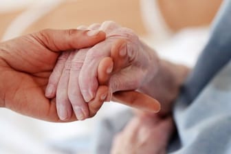 Eine Pflegerin hält in einem Altenheim die Hand einer Bewohnerin.