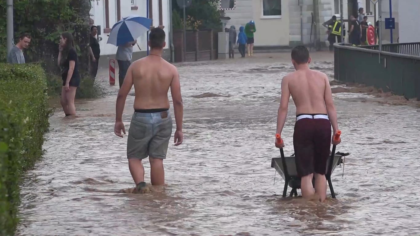 Hessen, Etzen-Gesäß: Männer waten mit einer Schubkarre durch eine überflutete Straße: Die kleine Ortschaft im Odenwaldkreis ist am Donnerstagabend nach einem schweren Unwetter überflutet worden.